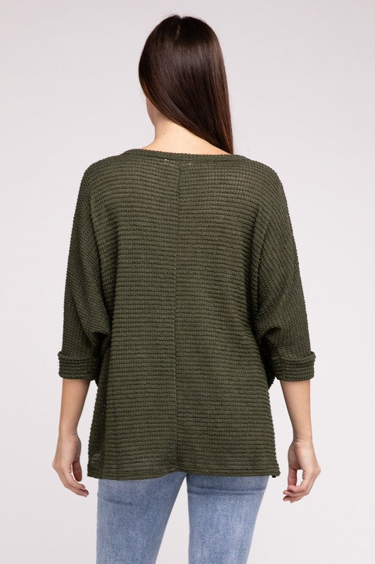 Back view of a model wearing a 3/4 sleeve jacquard sweater in olive green, paired with light jeans.