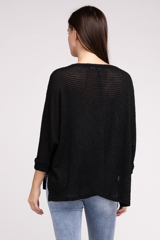 Back view of a woman wearing a black 3/4 sleeve hi-low hem jacquard sweater with rolled sleeves.