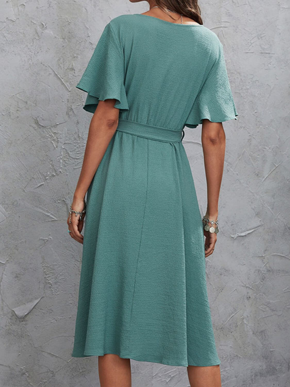 Woman wearing a teal Surplice Flutter Sleeve Midi Dress with a tied waist, viewed from the back.