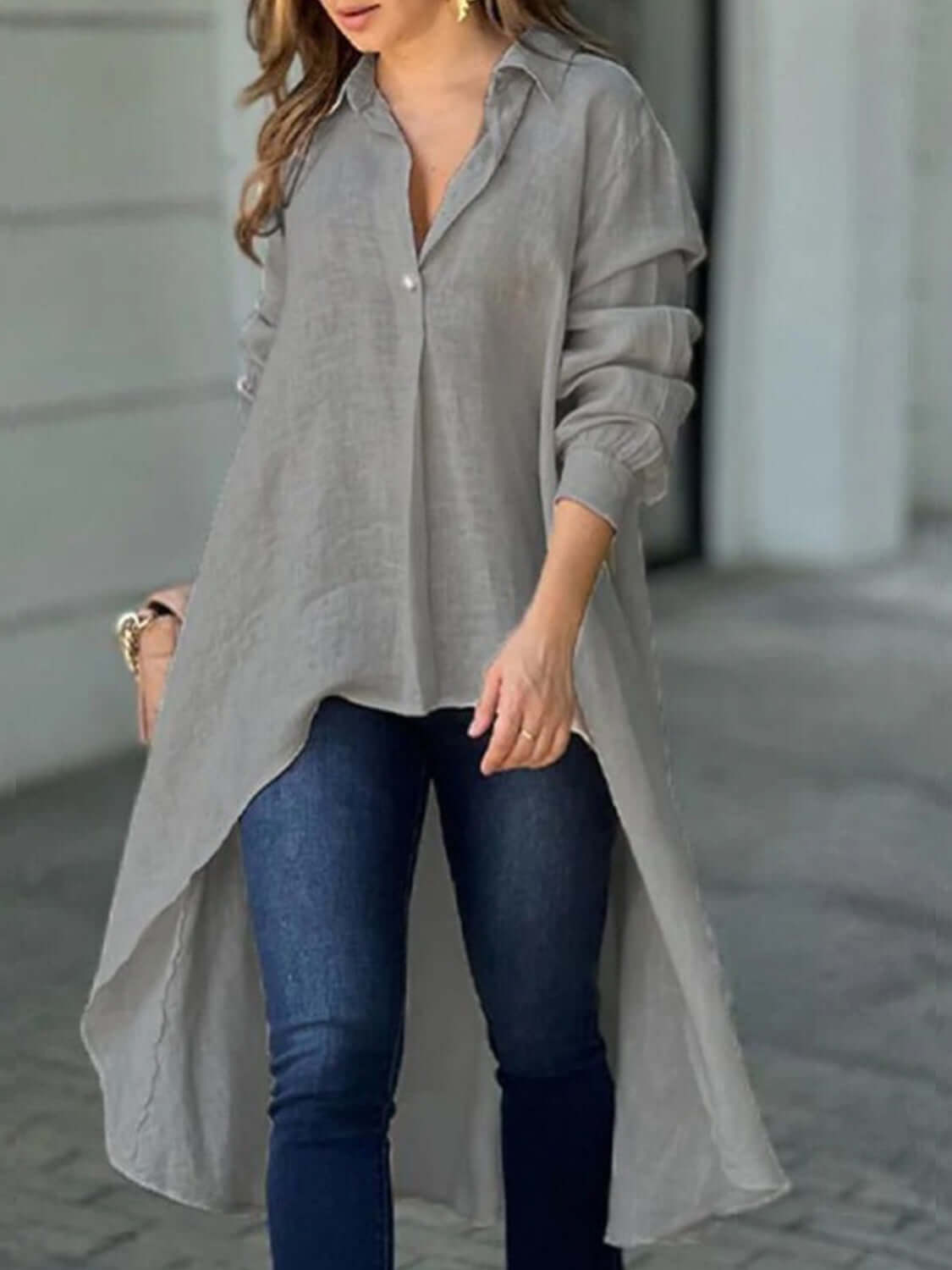 Woman wearing a full-size high-low collared neck long sleeve shirt in gray with buttoned front, paired with blue jeans.