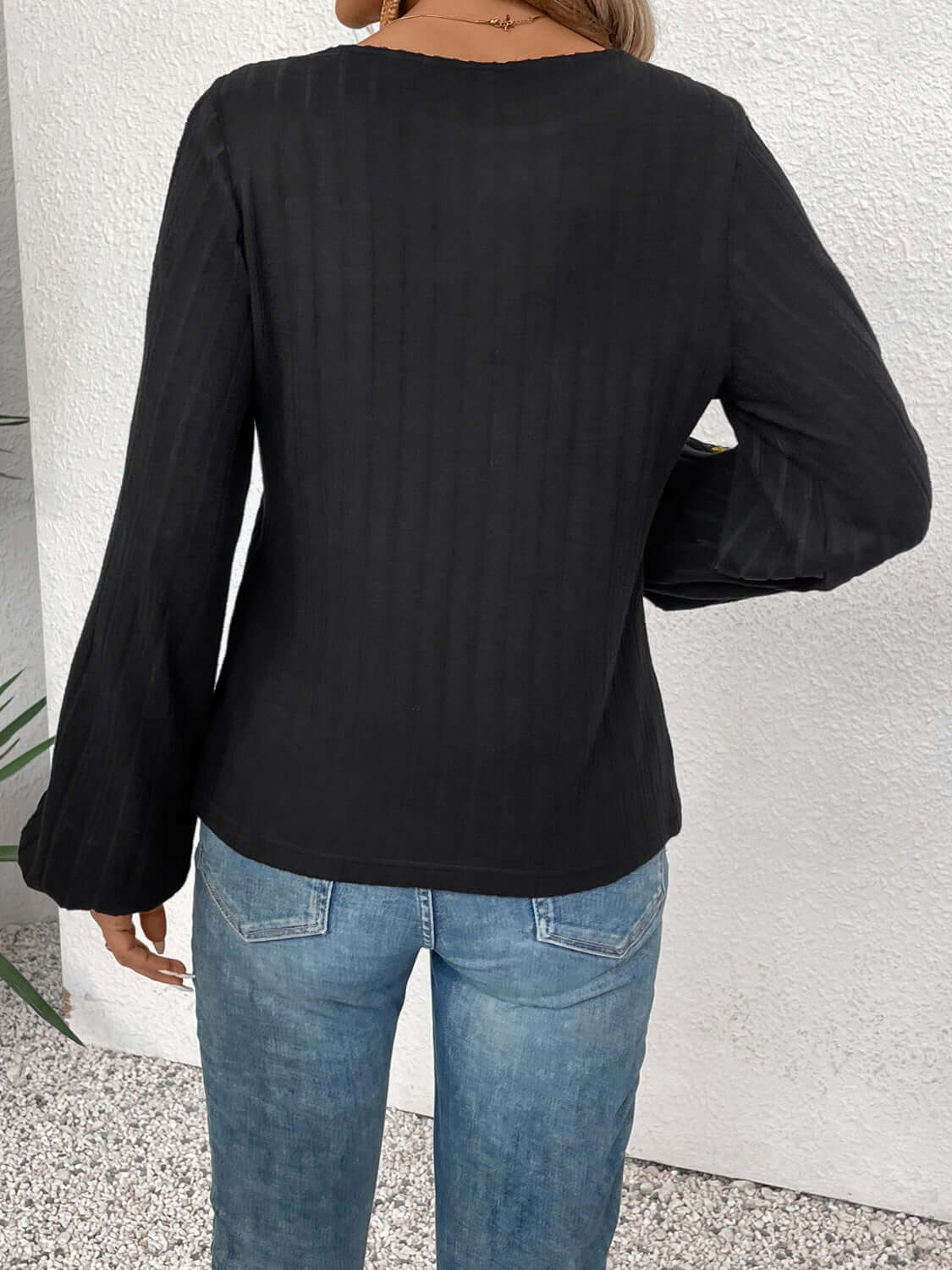 Embroidered round neck long sleeve blouse in black, shown from the back with moderate stretch and paired with blue jeans.