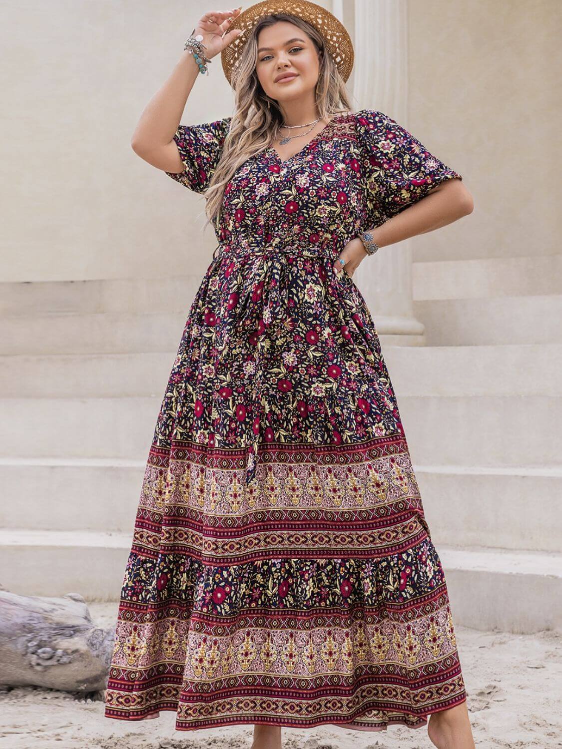 Plus size woman in a printed V-neck short sleeve maxi dress with a tied waist, standing outside.