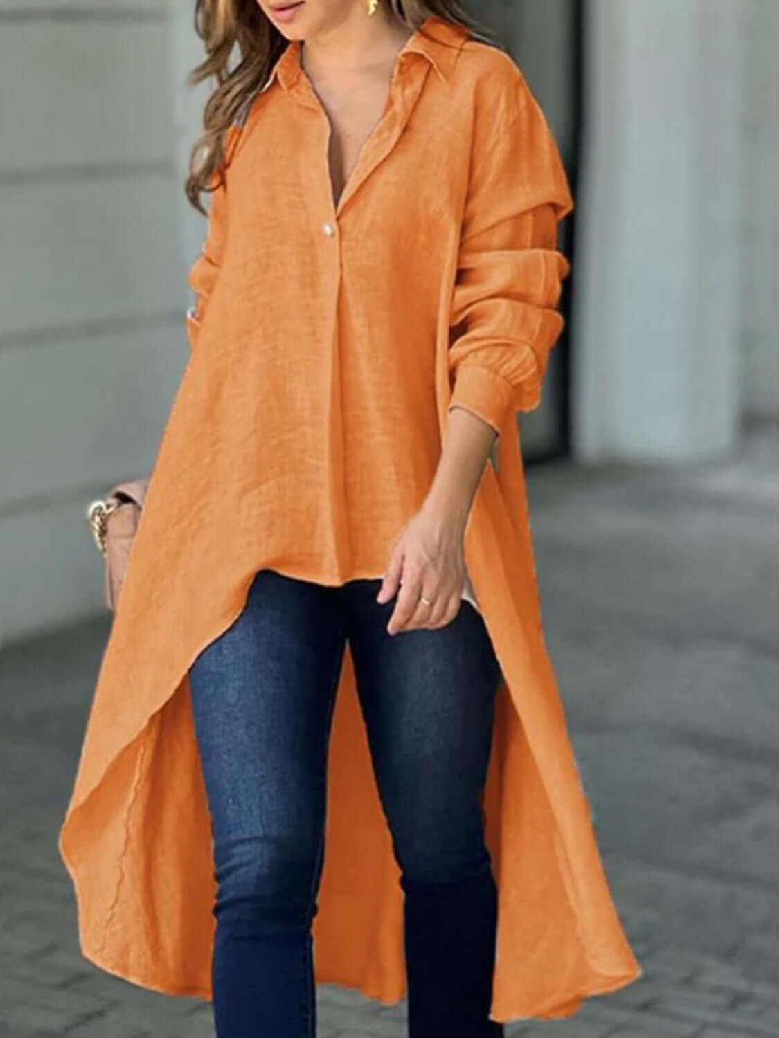 Woman wearing an orange full-size high-low collared neck long sleeve shirt with buttoned front, paired with blue jeans.