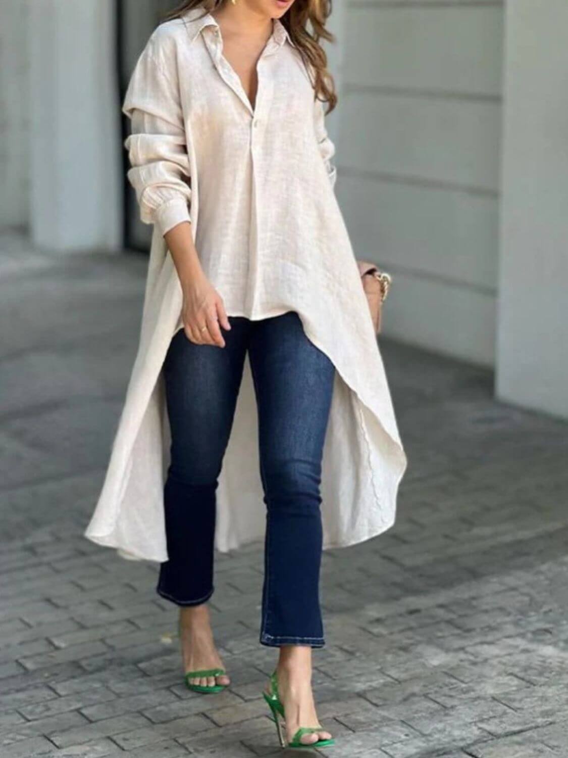 Woman wearing full-size high-low collared neck long sleeve shirt with buttoned front, paired with blue jeans and green heels.