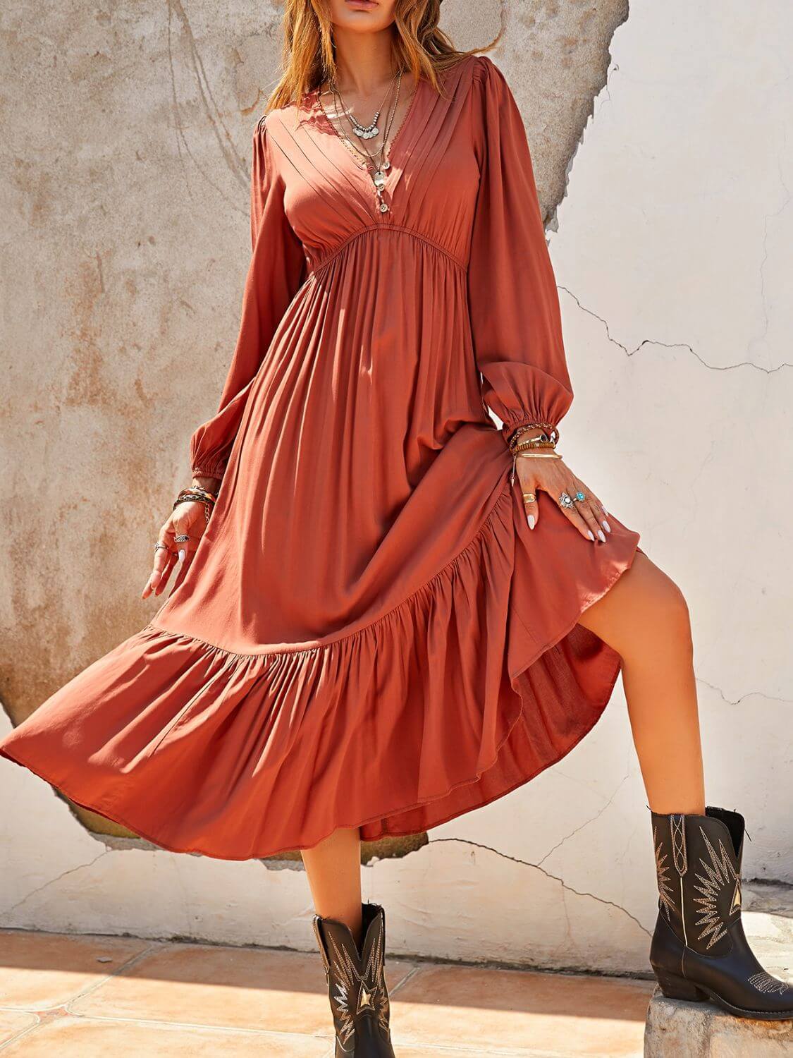 Woman wearing ruched V-neck long sleeve midi dress in rust color paired with black boots, ruffled hem detailing, and accessories